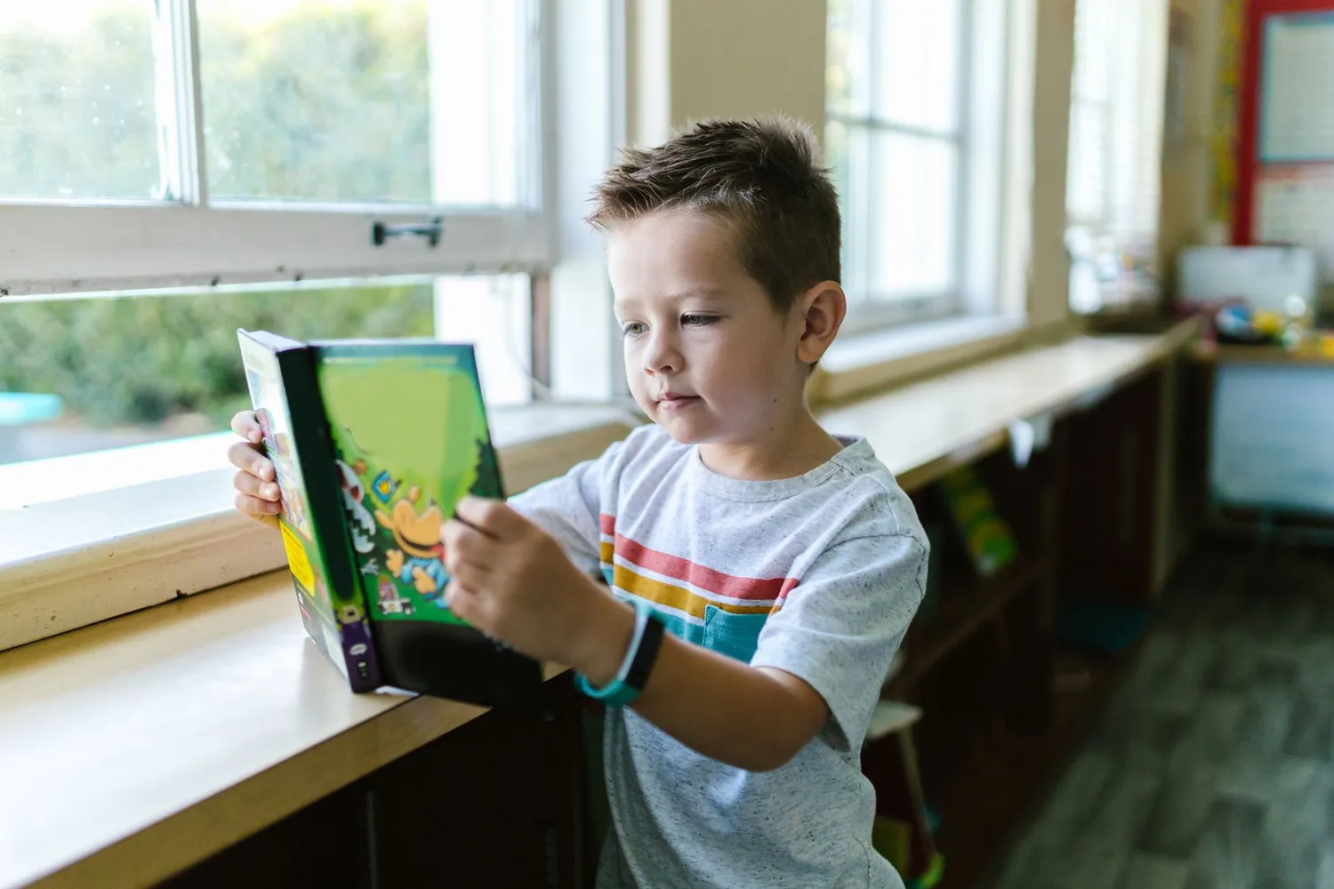 A young student reading a book in a bright classroom
